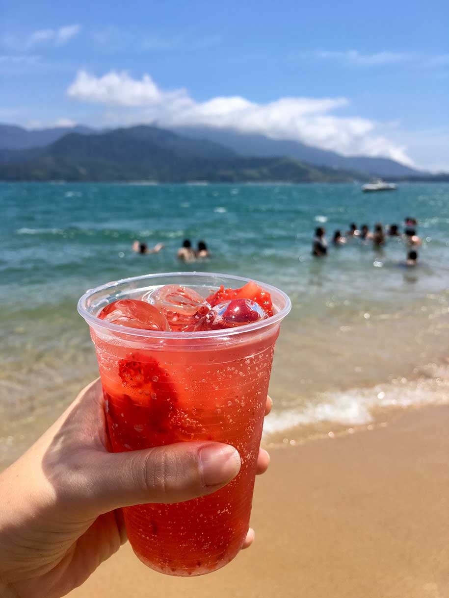 copo com caipirinha de morango e vista para a praia, em ilhabela